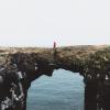 Person crossing a natural rock bridge above the sea
