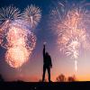 Person holding a sparkler with fireworks in the background